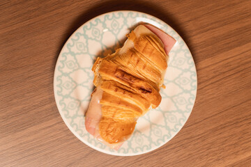 Top view of a croissant with ham and cheese on a wooden table.
