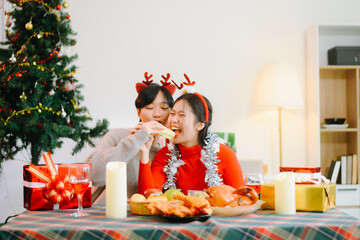 Smiling Asian couple celebrating Christmas together, wearing Santa hats and taking a romantic selfie at a festive dinner table with gifts and candles.