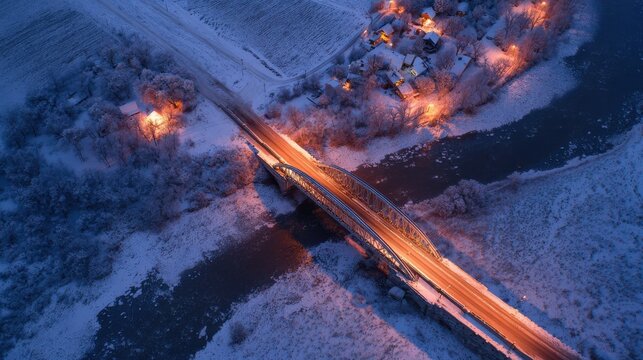 aerial view of snowcovered bridge against frosty landscape illuminated by warm lights from nearby houses in the evening twilight