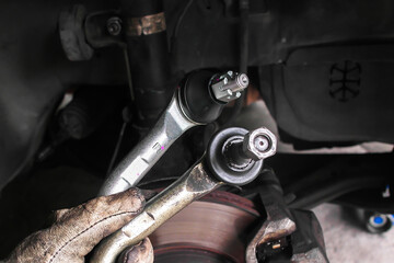 Mechanic holding new and old outer tie rod ends for car steering system replacement, automotive suspension repair, comparison of worn and new parts during maintenance and vehicle alignment work