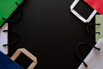 Black Friday concept with colorful shopping bags with handles border a dark background for sales and promotions.