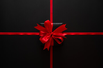 Black Friday concept with red ribbons cross a dark background with a black gift and red bow for sales headers.