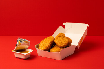 Chicken nuggets in a paper container and yellow dipping sauce.  紙容器に入ったチキンナゲットと黄色のディッピングソース（マスタードソースなど）。