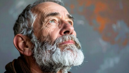 Portrait of old man with beard looking up against a gray background.