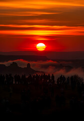 Fototapeta premium Fiery Sunset Silhouette. Crowd of Figures Against Intense Red and Orange Flames