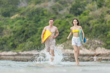 Happy young couple running with surfboards in hand along tropical beach shoreline, splashing water, enjoying summer fun and adventure. Great for lifestyle, travel, and vacation themes.