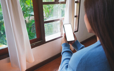 Mockup image of a woman holding mobile phone with blank desktop screen at home