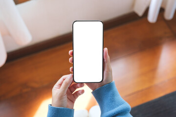 Top view mockup image of a woman holding mobile phone with blank desktop screen at home