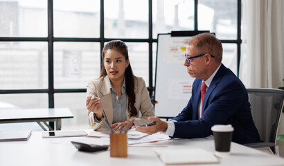 Two colleagues are sitting at the meeting room and discussing charts financial report and statistics.
