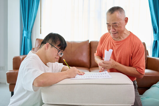 A man with Down syndrome is sitting at home doing his math homework with his teacher
