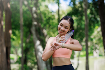 Fototapeta premium Woman checking smartwatch after hydrating during a workout in a green park, focusing on health and active lifestyle