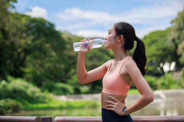 Young woman hydrating with a plastic water bottle after workout in a park, focusing on health and...