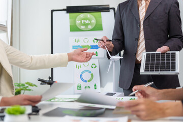 Business professionals discussing sustainability and green energy solutions, using a solar panel and wind turbine model during a meeting