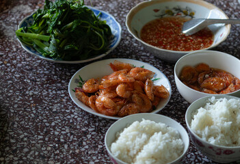 A rustic Vietnamese family meal spread with steamed rice, cooked shrimp, boiled water spinach, and traditional chili garlic dipping sauce.