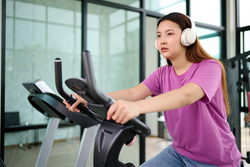 Obraz premium A woman exercising on a stationary bike while wearing headphones, indicating a focus on fitness and health
