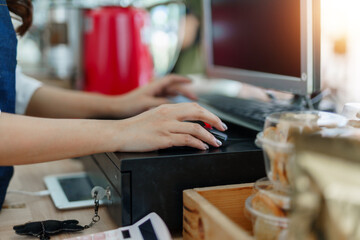 Female hands operating a computer mouse, working at a retail checkout counter in a small business or cafe setting