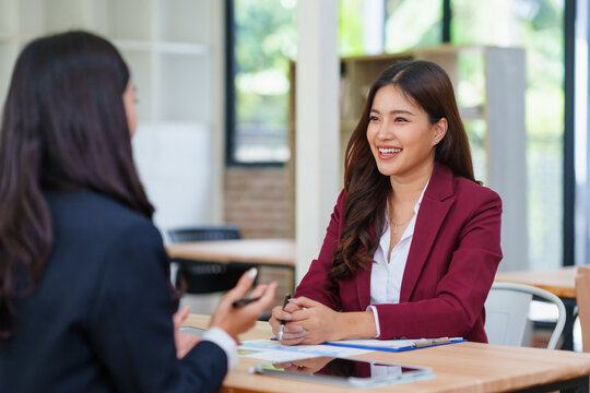Two professional businesswomen having a conversation during a job interview or mentoring session at a modern office desk