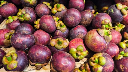 Fresh mangosteens piled together in a market display. The purple rind and green stems highlight tropical fruit freshness, natural texture, and organic produce perfect for healthy food concepts.