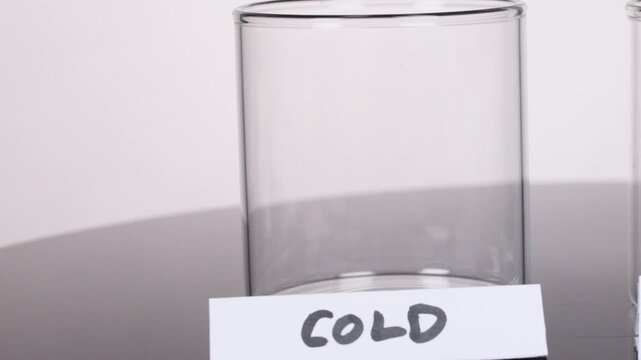 Hand Places 'Cold' Label on Empty Glass Beaker in Lab