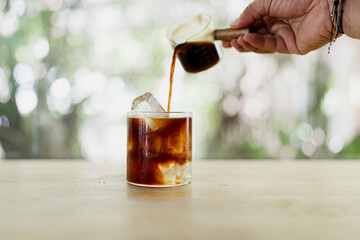 One shot of pure coffee poured into with ice and water against nature background.