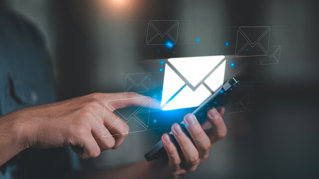 A person using a smartphone with glowing email icons, representing digital communication, online messaging, email marketing, business contact, and modern technology connection.