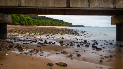 A stone littered tropical beach fringed with rainforest jungle trees almost reaching the sea, as...