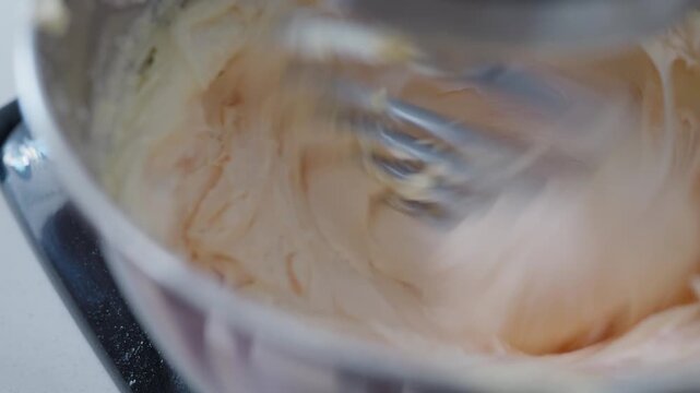 Close up, Pink food dye being dropped into white whipping buttercream in a stand mixer stainless steel bowl with a paddle attachment.