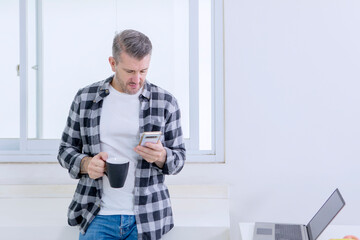 Casual Middle-aged Man Checking His Smartphone While Taking a Coffee Break From Working on His...