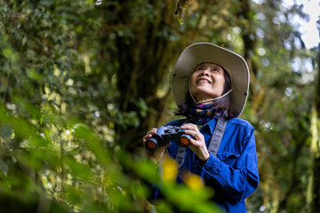 Bird watcher is looking through binoculars while exploring in the pine forest for surveying and discovering the rare biological diversity and ecologist on the field study concept