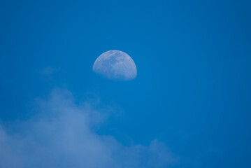 La Luna visible durante el día entre nubes y cielo azul. Luna en fase creciente visible durante el día, sobre un cielo azul con ligeras nubes.