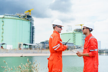 Refinery engineers discussing data on digital tablet at oil plant.