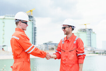Refinery engineers shaking hands after project success at oil plant.