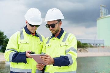 Refinery engineers discussing data on digital tablet at oil plant.
