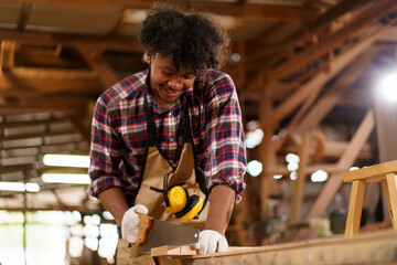 African American carpenter sawing wood with hand saw in sawmill factory