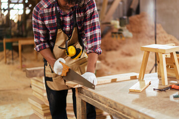 African American carpenter sawing wood with hand saw in sawmill factory