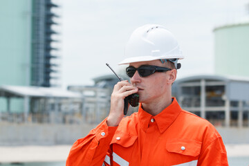 Engineer at oil refinery uses walkie-talkie for inspection.