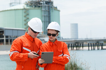Male and female engineers discussing data on tablet at oil refinery.