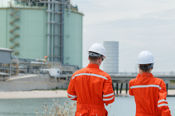 Refinery engineers discussing data on digital tablet at oil plant.