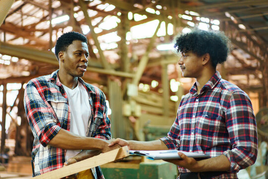 African American carpenters shaking hands in sawmill and wood factory.