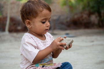 a Curious Toddler Sitting Outdoors and Holding a Stone While Playing in a Rural Setting