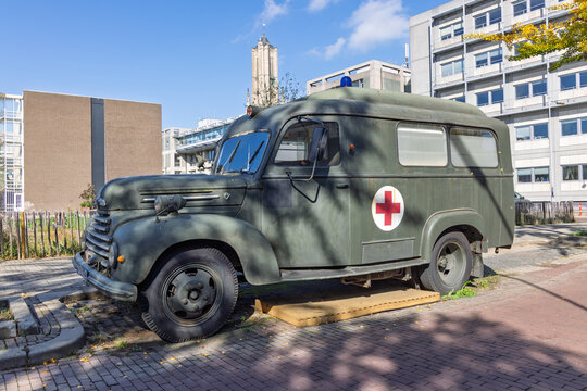 A vintage green ambulance with a red cross emblem, from the military, parked on a street in a Dutch city environment. - Powered by Adobe