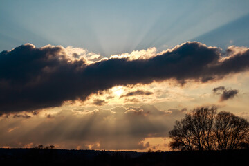 Golden sunbeams pierce through heavy clouds, painting the sky with striking crepuscular rays above a silhouetted horizon at dusk
