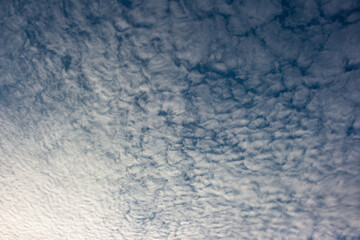 Textured white clouds drift across the blue expanse, creating a serene, rippled pattern. This stunning cloudscape provides an airy, abstract backdrop