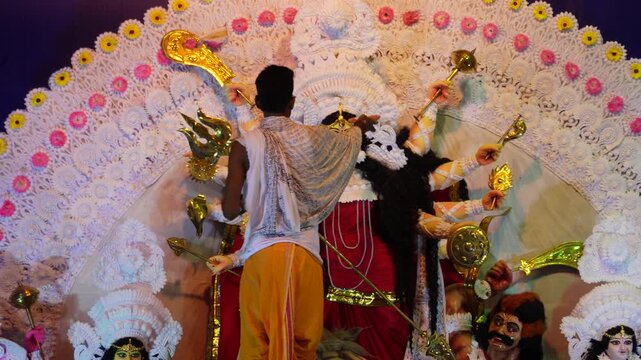 Hindu priest or panditji performing a ritualistic puja for a large idol of Goddess Durga.
