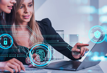 Two women working together on a laptop, with digital security icons overlayed, futuristic style, in a modern bright office. Concept of cybersecurity teamwork
