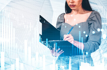 Woman writing on clipboard with digital financial graphs overlay, modern office background, concept of analysis, business planning, and strategy