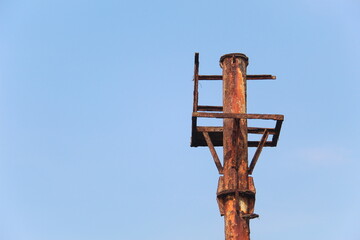 Close-up of an old rusty metal pole structure against clear blue sky. Industrial decay, weathered steel, and minimal composition showing texture, corrosion, and aging over time in outdoor environment