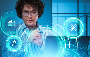 Man with curly hair and glasses working at laptop, digital holographic interface with icons and data analysis, blue office background, technology concept
