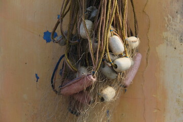 Close-up of fishing net with white and pink floats hanging against a weathered wall. Ideal for maritime, fishing, rustic, or traditional-themed visual conten