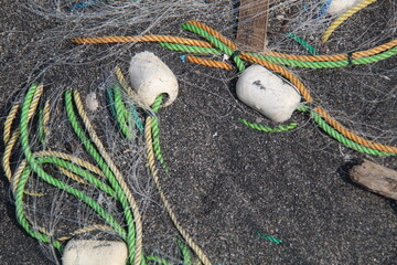 Close-up of colorful fishing ropes and nets with white floats on dark sand. Detail of traditional fishing equipment used by coastal fishermen after a day at sea